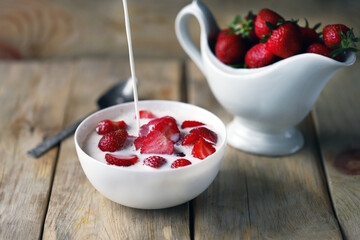 A stream of milk is poured into a bowl of strawberries. Cooking strawberry dessert with milk.