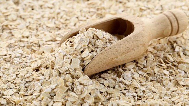 Heap of oat flakes rotating with wooden scoop, cereal breakfast or food concept