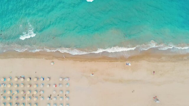 Top Down Drone View of Beach Umbrellas on Sand and Sea Waves at Summer Vacation or Holiday on Crete Island in Greece. Tourism and Travel in Tropical Country Resort. Aerial 4K Wide Pan Right Shot