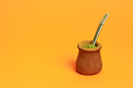 argentine wooden mate cup on orange background with yerba mate inside and straw