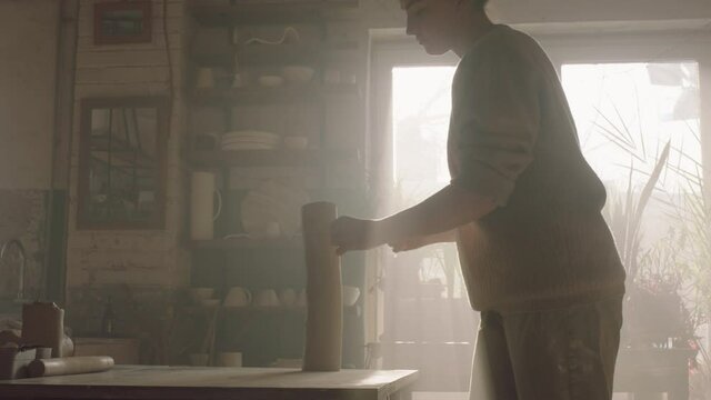 Woman potter is standing at workplace in workshop and cutting clay with string tool into smaller pieces, works with inspiration on new project, Slow motion.