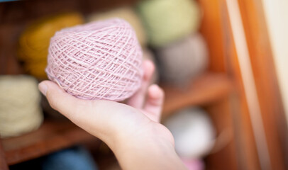 Female hand holding the pink yarn ball with the earth tone yarn in the wooden cupboard  prepare for made Crochet and knitting