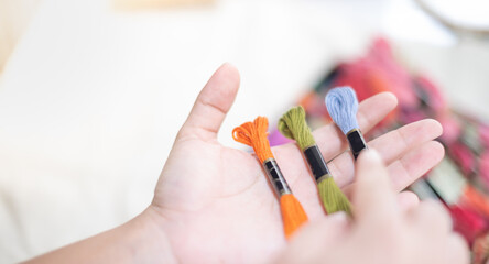 Close up hands of tailor woman holding many threads of different colors on table and prepare to use with white cotton and frame wood.