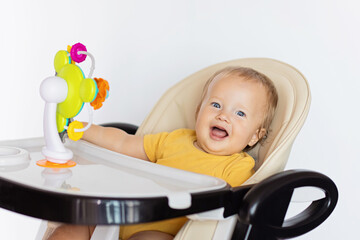 Cute caucasian infant girl ten months old sitting in baby chair and playing with educational colorful plastic toy isolated on white background 