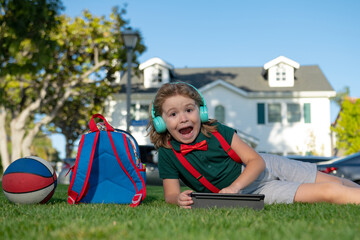 Kid with tablet device sitting outdoor in garden, wearing short and shirt. Lttle child outdoor school, education, on line distance learning.