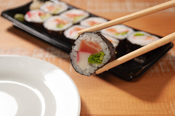 A pair of chopsticks holding one sushi over ponting to a small plate and a sushi bar in the background