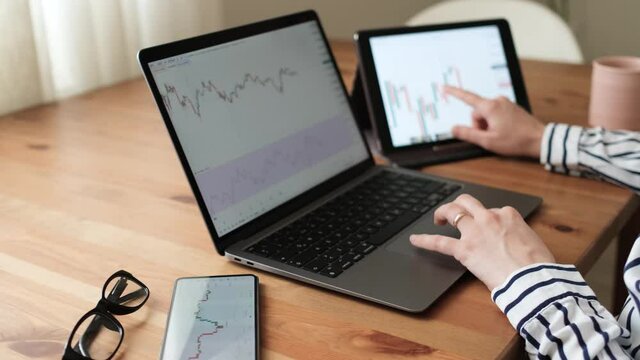 Entrepreneurial business woman researching stock market opportunities. Woman examining graphics in detail with her mobile phone, tablet and laptop at home. woman who follows the stock market for easy 