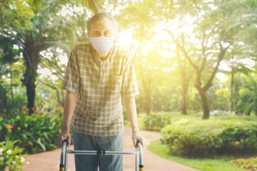 Elderly man in face mask steps with walker at park