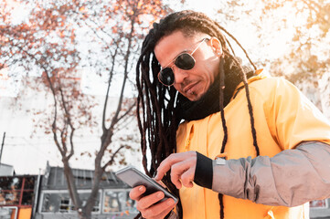 young brown-skinned hispanic latino guy checking his phone on the street on a sunny morning