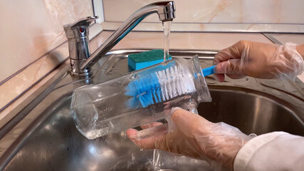 Woman washes glass jug in kitchen sink.  Close up of pitcher, faucet and female hand in gloves....