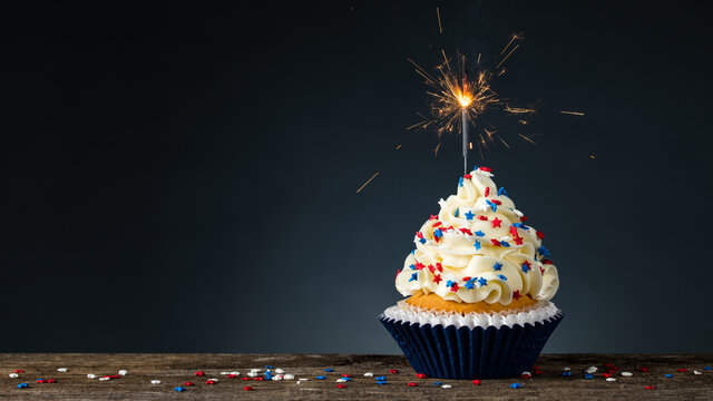 Birthday Cupcake American style. Sparkler light burning in a cake. 4th of July, Independence, Memorial or Presidents Day. Tasty cupcakes with white cream icing and colored stars sprinkles. Copy space