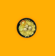 Indonesian Warm noodles served with fresh tomatoes and meatballs in a round bowl on black and pickles on a white bowl on a orange background