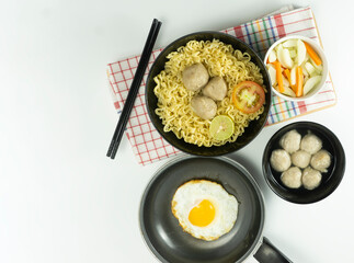 Indonesian Warm noodles served with eggs and fresh tomatoes with meatballs on a black bowl and pickled on a white bowl and eggs on a white background