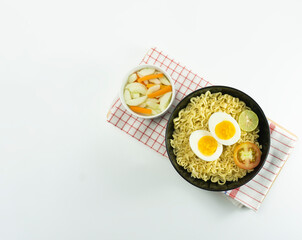 Indonesian Warm noodles served with fresh tomatoes and meatballs in a round bowl on black and pickles on a white bowl on a white background