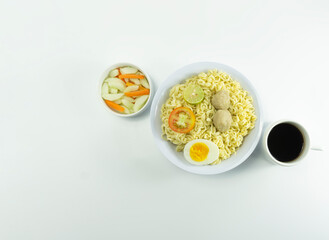 Indonesian Warm noodles served with fresh tomatoes and meatballs on a white round bowl and pickles on a white bowl on a white background