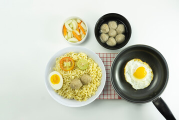 Indonesian Warm noodles served with fresh tomatoes and meatballs on a white round bowl and pickles on a white bowl on a white background