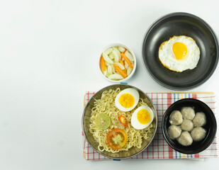 Indonesian Warm noodles served with fresh tomatoes and meatballs on a white round bowl and pickles on a white bowl on a white background