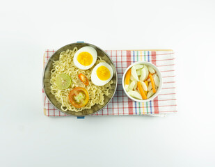 Indonesian Warm noodles served with fresh tomatoes and meatballs on a white round bowl and pickles on a white bowl on a white background