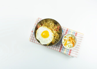 Indonesian Fried rice served with fresh tomatoes and meatballs in a stainless round bowl and pickles on a white bowl on a white background