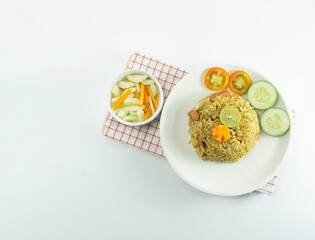 Nasi goreng or Indonesian Fried rice served with fresh tomatoes and meatballs on a white ceramic plate and pickles on a white bowl on a white background