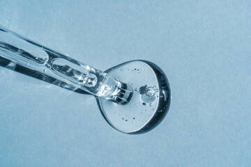 A cosmetic product on a blue background flows out of a pipette with bubbles