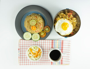 Fried rice served with fresh tomatoes and meatballs in a green tosca ceramic plate and pickles on a white bowl on a white background