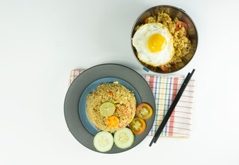 Fried rice served with fresh tomatoes and meatballs in a green tosca ceramic plate and pickles on a white bowl on a white background