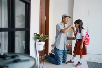 portrait of indonesian primary school female student shake and kiss her father's hand before going...
