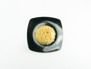 Nasi Goreng or Indonesian Fried rice served with fresh tomatoes and meatballs in a black tosca plate and pickles on a white bowl on a white background