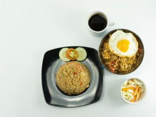 Nasi Goreng or Indonesian Fried rice served with fresh tomatoes and meatballs in a black tosca plate and pickles on a white bowl on a white background