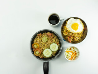 Nasi Goreng or Indonesian Fried rice served with fresh tomatoes and meatballs in a teflon bowl black tosca and pickles on a white bowl on a white background