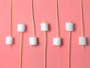 White marshmallow on wooden sticks on a pink background. Concept of glamping, glamours way to go...