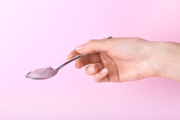Female hand with spoon of tasty yogurt on color background