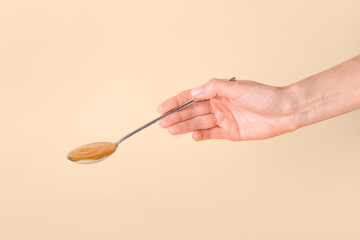 Female hand with spoon of tasty apricot jam on color background