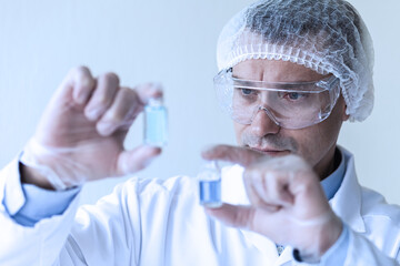 Young man scientist in glasses and gloves working on laboratory test of blue liquid in tube, chemistry science, medical biology experiment technology, pharmacy development solution. Close up