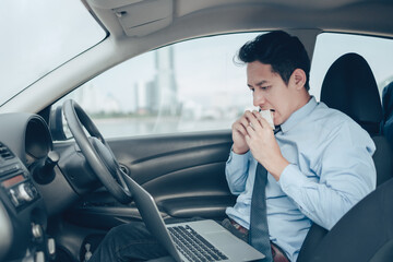 Businessman eating sandwich while working in laptop in the drivers seat in his car. Busy businessman and food in car.
