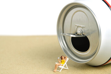 Miniature people toy figure photography. Creative summer vacation concept. Girl chilling at beach chair in front of soft drink canned.