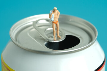 Miniature people toy figure photography. Creative summer vacation concept. A men standing above soft drink canned getting ready to swim.