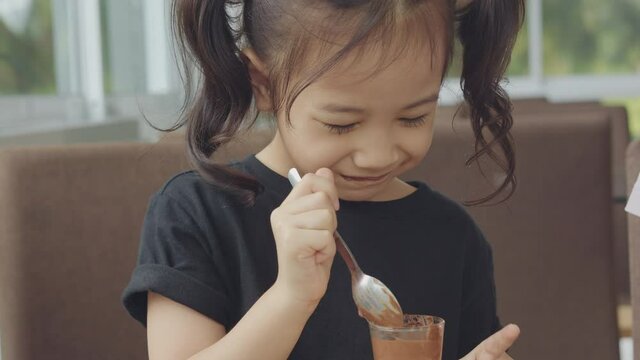 Close up portrait 4K of adorable 5 years old asian girl with black hair is eating sweet chocolate moose with happy, enjoy and funny emotion and express tasty and delicious shows dirty mouth. 