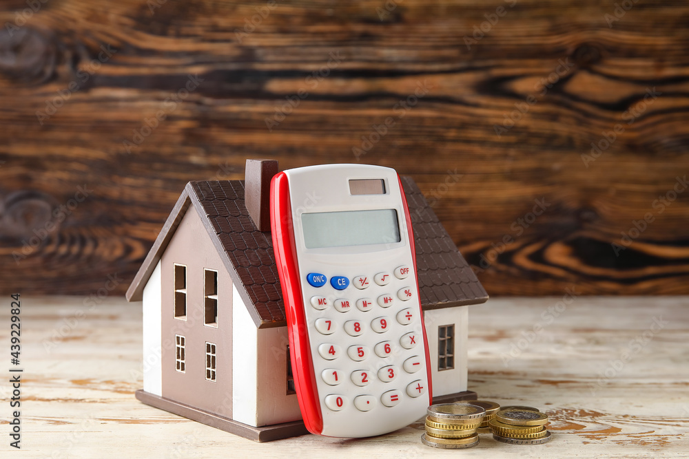 Sticker calculator with house model and coins on wooden background