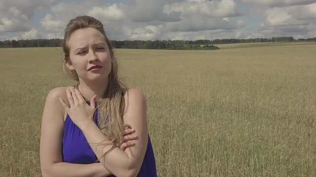 a girl in a blue dress performs a sad song in a field. Singing in nature. Shooting the clip outdoors. face close-up
