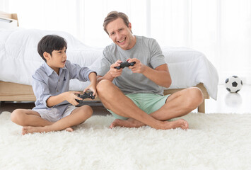 Father and his mixed-race son holding controller joystick to play a game together with fun and happy in bedroom