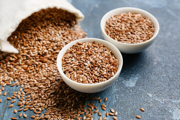 Bag with bowls of flax seeds on color background, closeup