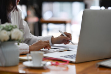 Fototapeta premium Cropped shot businesswoman sitting in front of laptop and analyzing business data in office.