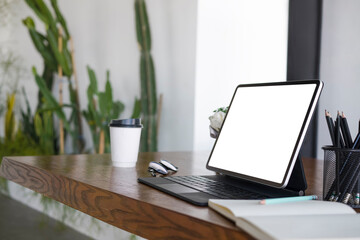 Computer tablet, notebook, coffee cup and pencil holder on wooden table.