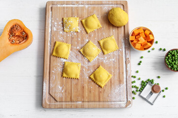 Wooden board with raw ravioli on white table
