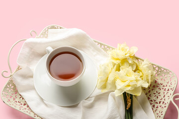 Tray with cup of tea and beautiful narcissus flowers on color background