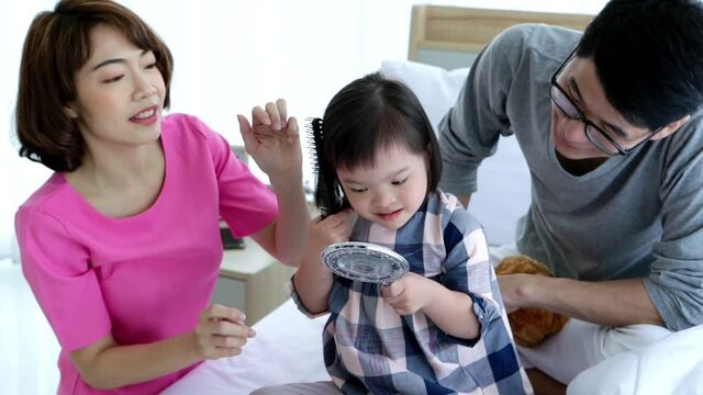 Slow motion of happy cheerful asian family of three father mother little daugther hanging out together on the bed. Little girl brushing her hair with holding mirror. 