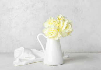 Pitcher with beautiful narcissus flowers on light background