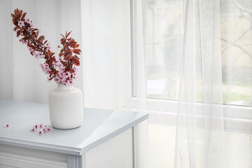 Vase with beautiful blossoming branches on table near window